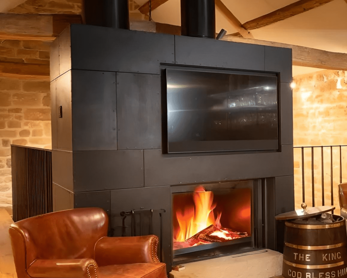 Blackened corten steel fireplace surround used as a chimney breast feature wall in a rustic interior.